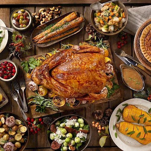 A Thanksgiving feast with roasted turkey, vegetables, stuffing, cranberries, pie, and various side dishes arranged on a wooden table.