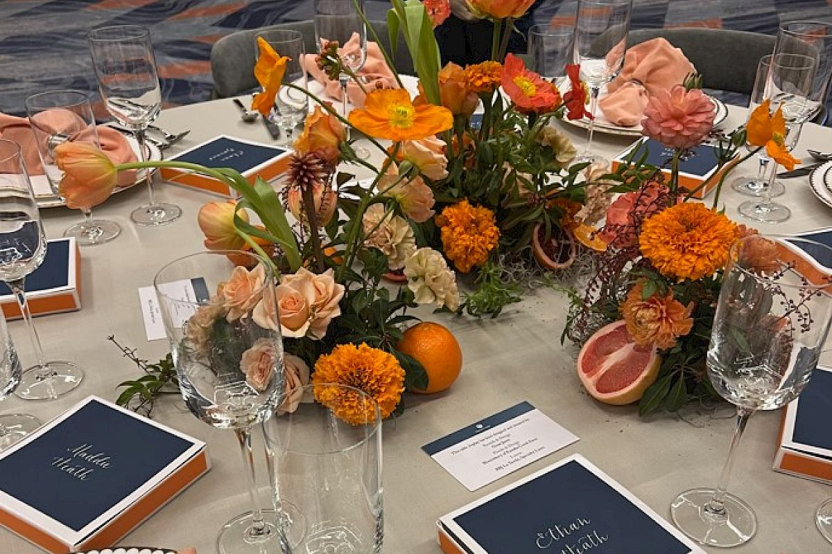 A beautifully set table with floral centerpieces, elegant tableware, and name cards, featuring shades of orange and peach.