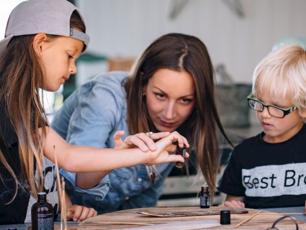 Three kids and a woman experiment with nail polish and tiny bottles, concentrating as they paint together.