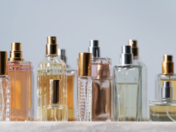 A row of elegant perfume bottles in various shapes and colors, with gold and silver caps, arranged on a light surface.