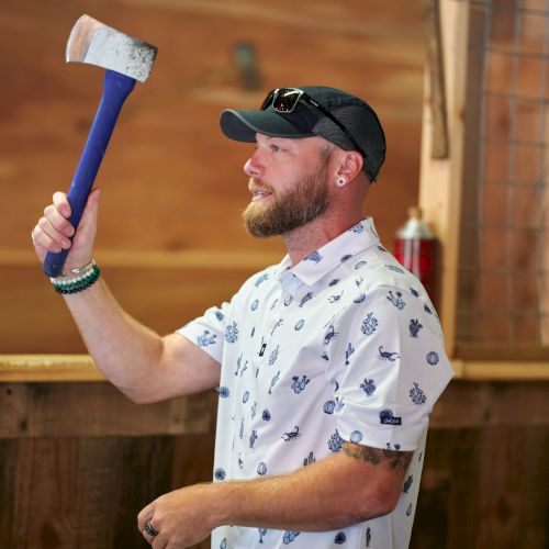 A man is standing in an axe-throwing area, holding an axe in a throwing position.