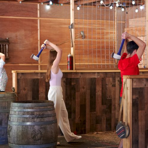 People are participating in an indoor axe-throwing activity, aiming at wooden targets with axes in a rustic setting.