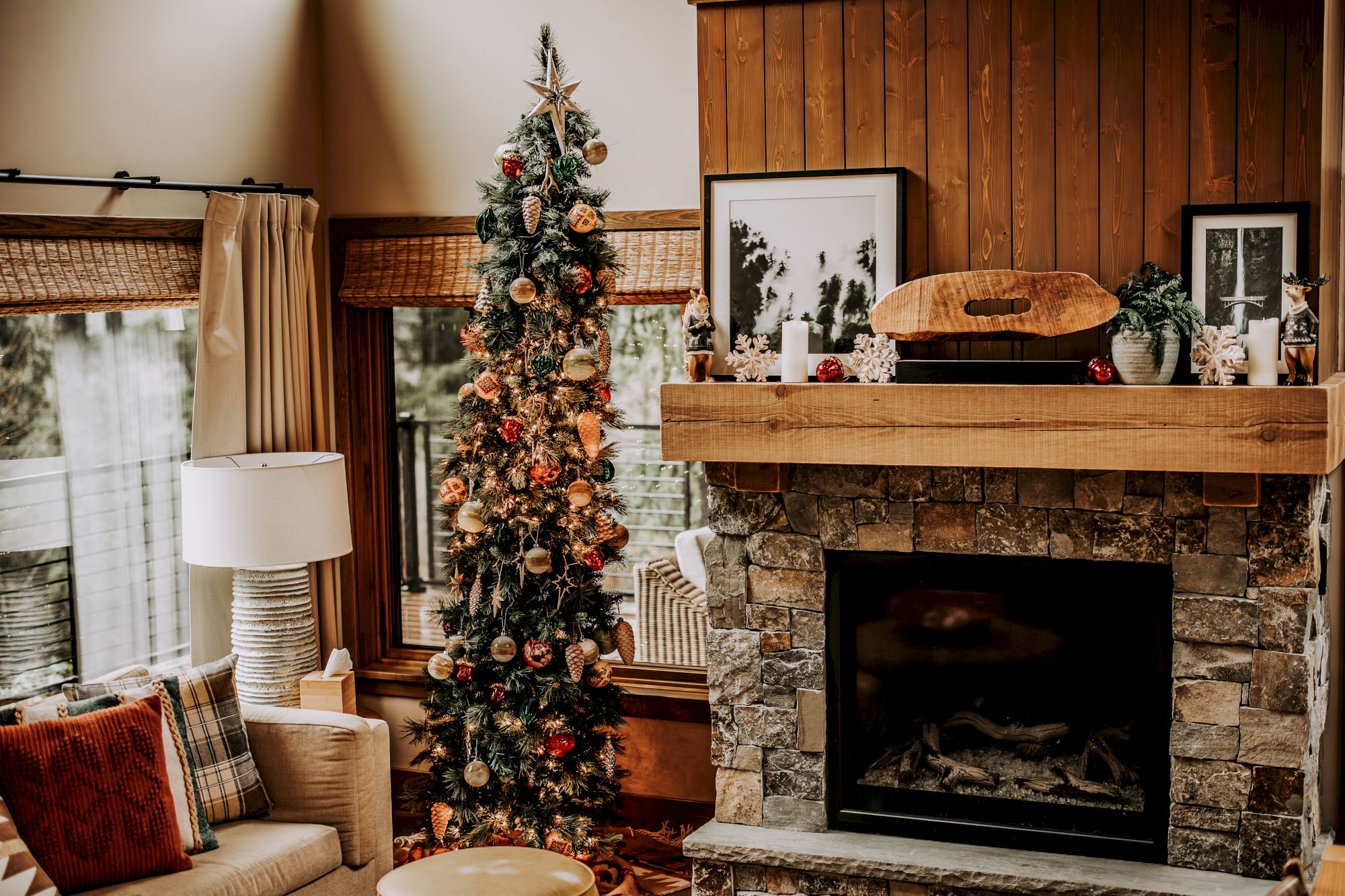 A warmly lit living room features a decorated Christmas tree beside a stone fireplace and holiday ornaments on the mantel.