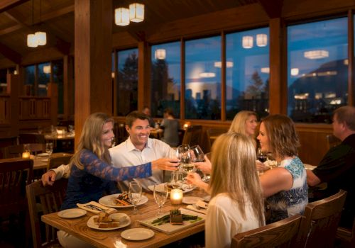 A group of friends cheers with wine glasses while dining together in a cozy, wood-paneled restaurant.