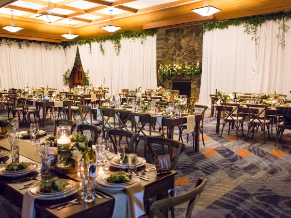 A decorated banquet hall with tables set for an event, featuring greenery, candles, and elegant table settings.