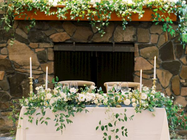 A decorated fireplace with greenery and a white table adorned with foliage and candles in a cozy setting.