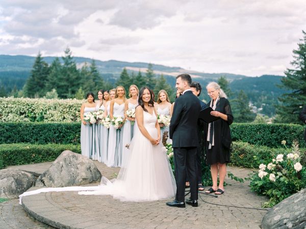 A wedding ceremony with a bride and groom standing together outdoors, bridesmaids holding bouquets, and an officiant present.