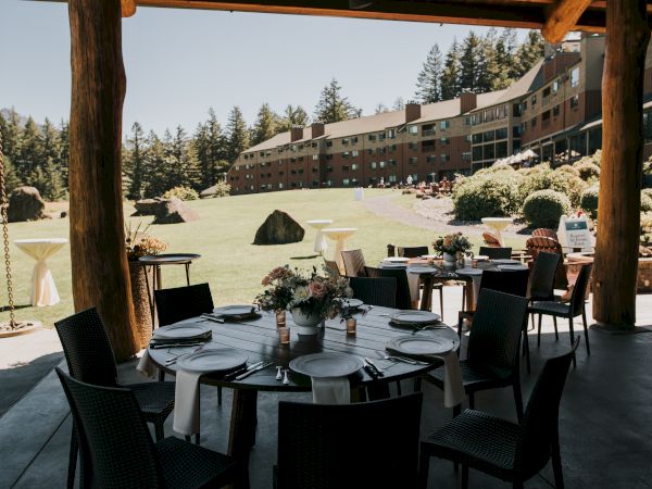 The image shows a decorated outdoor dining area with tables set, overlooking a grassy field and a large building in the background.