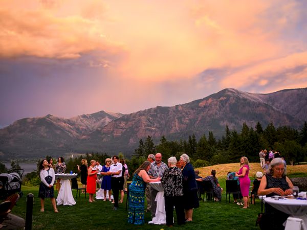 A group of people at an outdoor event with mountains in the background under a colorful sky.