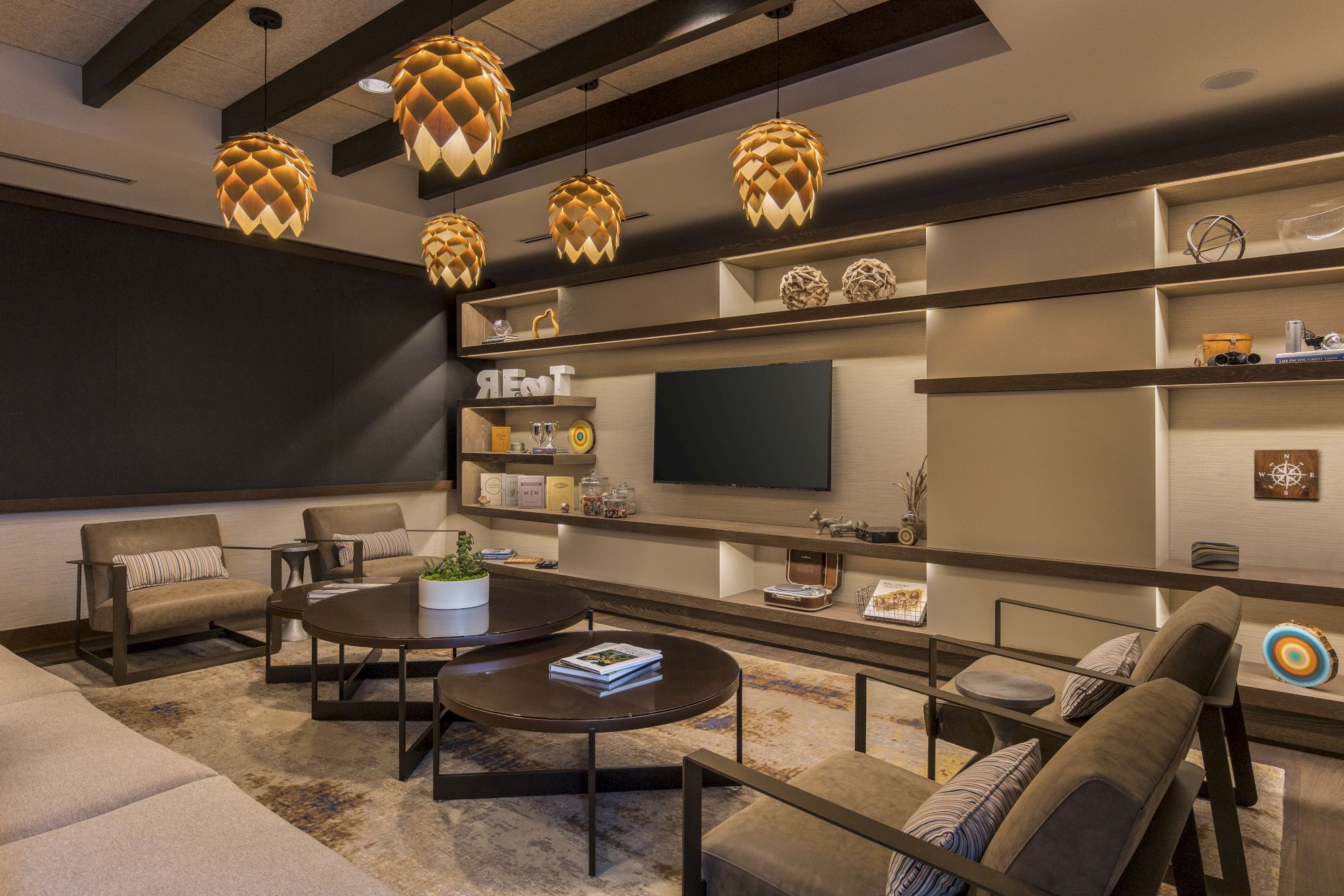 A cozy living room with modern furniture, decorated shelves, a TV, and unique pendant lights hanging from the ceiling.
