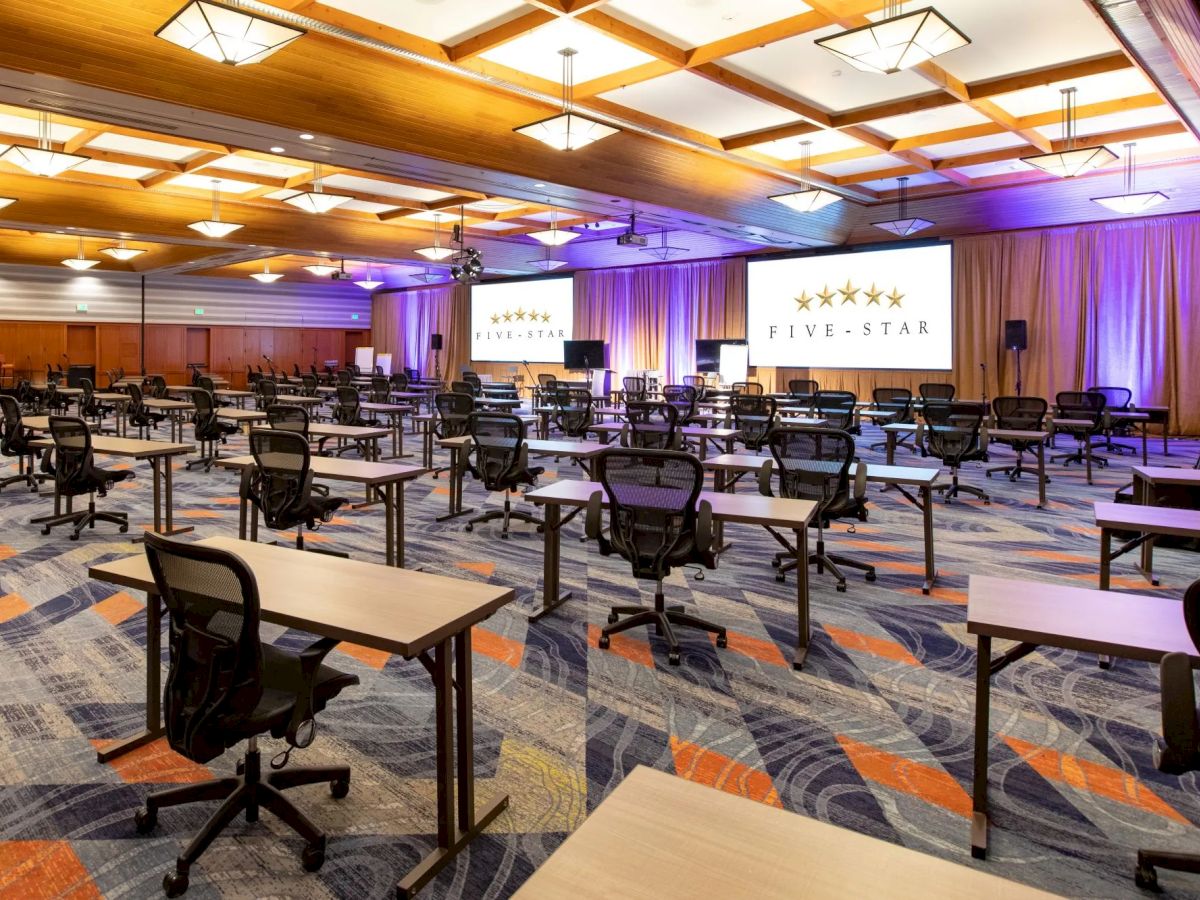The image shows a conference room setup with rows of tables and chairs, a stage, screens, and a "Five-Star" banner in the background.