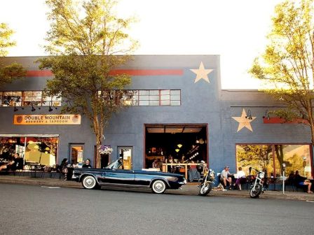 The image shows a brewery taproom with stars painted on the building, a vintage car, and motorcycles parked outside.