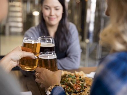 People are toasting with beer glasses over a table with food, likely sharing a meal and enjoying each other's company.