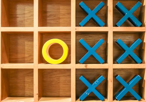 A wooden tic-tac-toe grid with blue Xs and one yellow O, forming a few Xs across but no clear winning line.