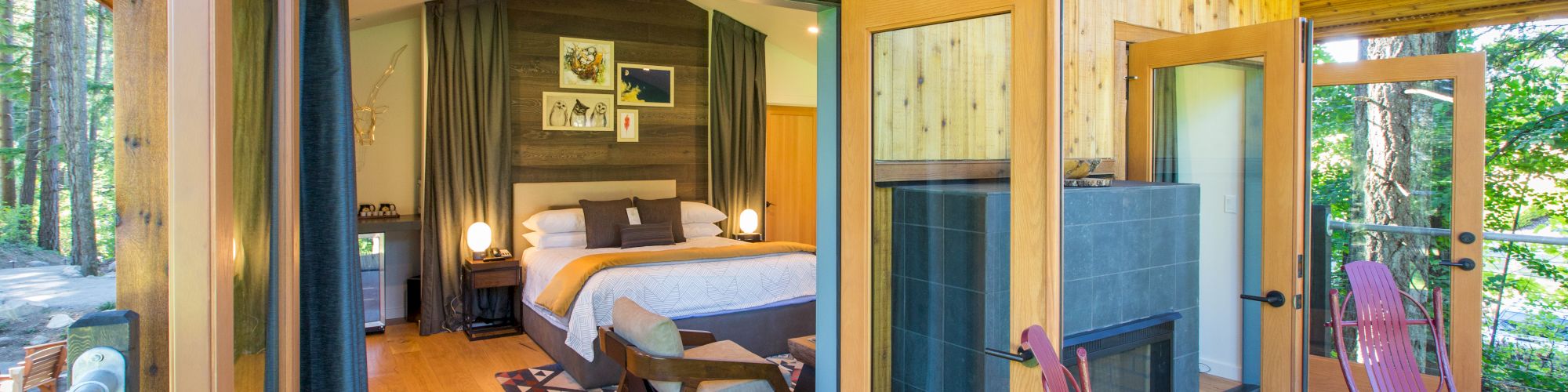 A cozy wooden cabin with open doors shows a furnished bedroom and an inviting patio with chairs surrounded by nature.