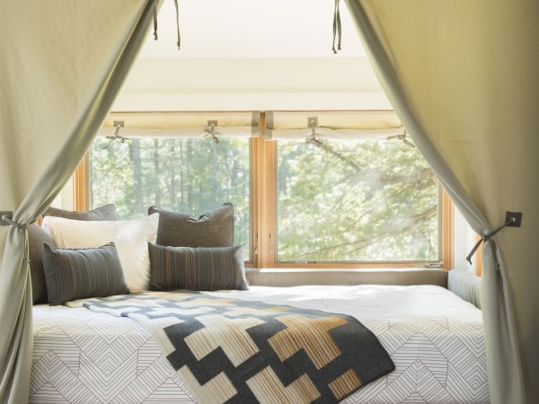Cozy bed with geometric blanket and pillows, enclosed by drapes; large window offers a view of trees outside.