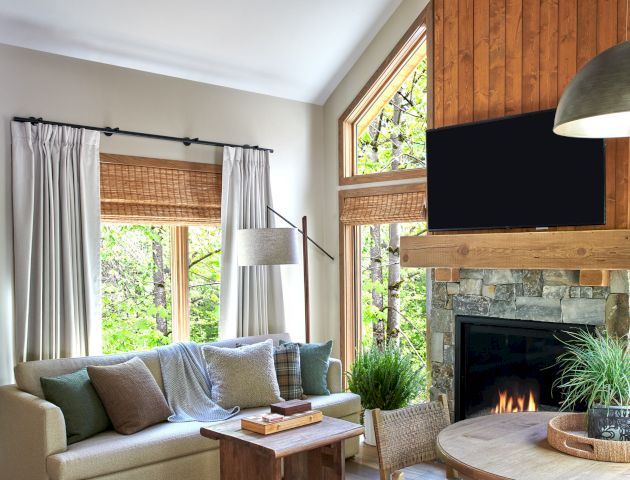 A cozy living room with a sofa, round dining table, fireplace, TV, and ceiling fan. Large windows bring in natural light.