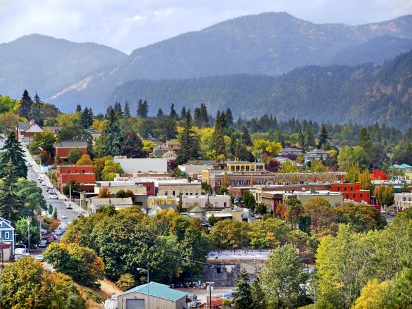 A scenic town with colorful buildings, surrounded by trees and mountains in the background, under a partially cloudy sky.