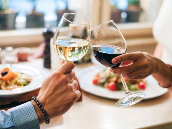 Two people clinking wine glasses over a table with plates of food, creating a celebratory or romantic atmosphere.