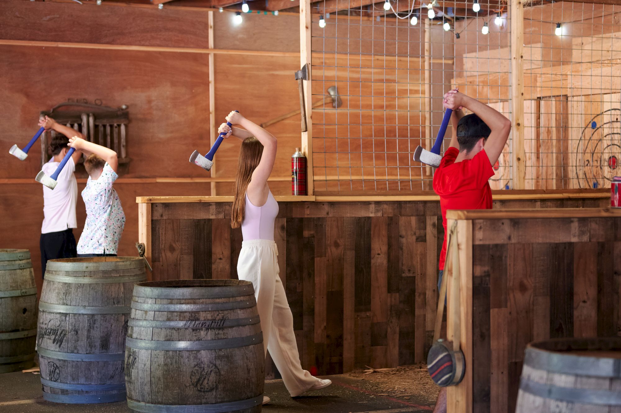 People are participating in an axe-throwing activity indoors, aiming at targets on wooden boards.