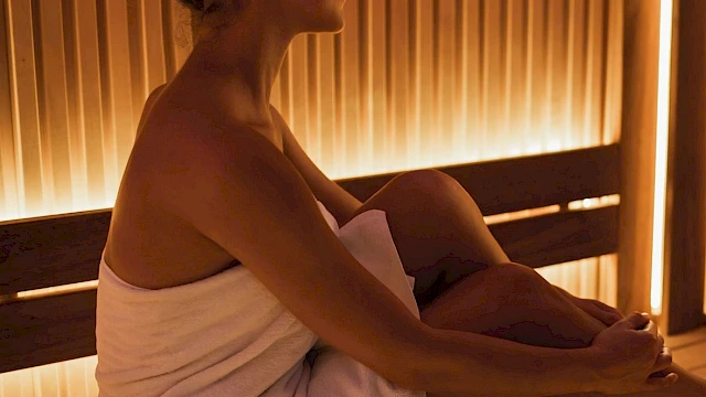 A person is sitting in a sauna wrapped in a towel, enjoying the warm, ambient lighting and relaxing environment.
