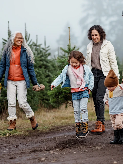A family of four with two kids walks hand-in-hand along a muddy path in a forested area, smiling and enjoying a outdoor hike together.