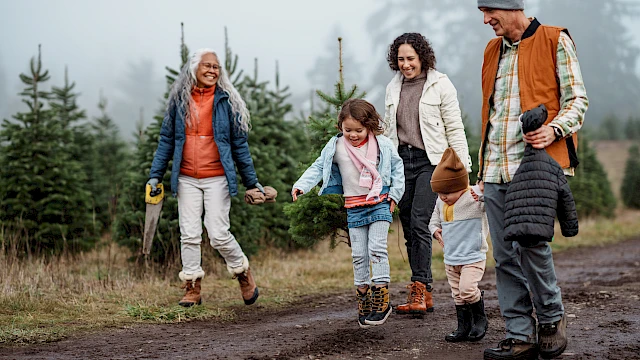 A family of four with two kids walks hand-in-hand along a muddy path in a forested area, smiling and enjoying a outdoor hike together.