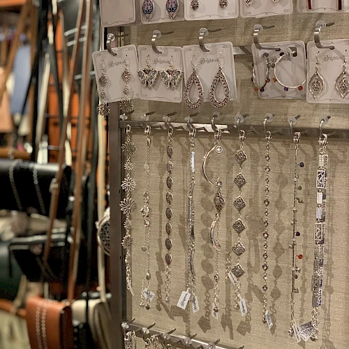 A jewelry display with dangling earrings and bracelets on a rack, silver pieces catching light, shoppers’ items in a shop.