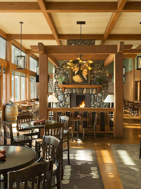 A cozy restaurant with wooden furniture, a stone fireplace, and large windows that let in natural light, creating a warm atmosphere.