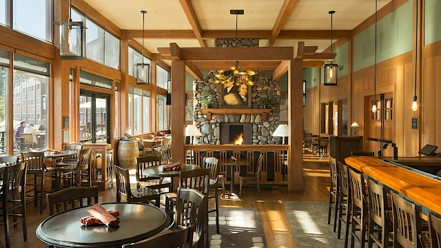 A cozy restaurant with wooden furniture, a stone fireplace, and large windows that let in natural light, creating a warm atmosphere.