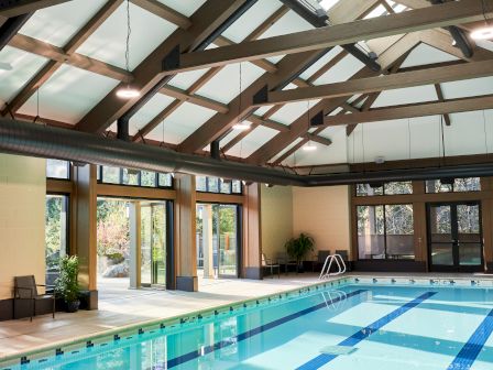 An indoor swimming pool with clear water, multiple swimming lanes, and a high ceiling with skylights allowing natural light.