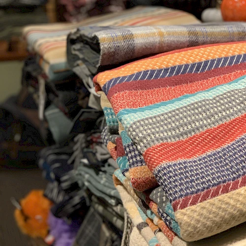 A stack of colorful woven blankets and textiles neatly folded on a display rack in a shop.